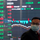A man in a mask in front of a markets board.